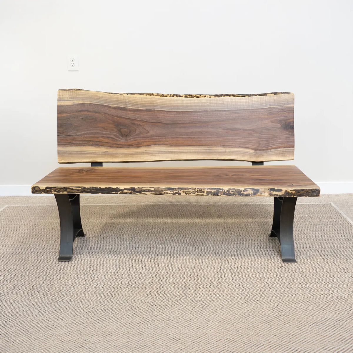 Live edge wood bench with black metal legs on light carpet, set against a white wall.