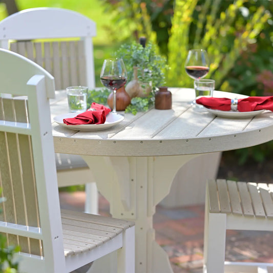 Round outdoor table with three chairs, red napkins, drinks, and a small plant centerpiece.