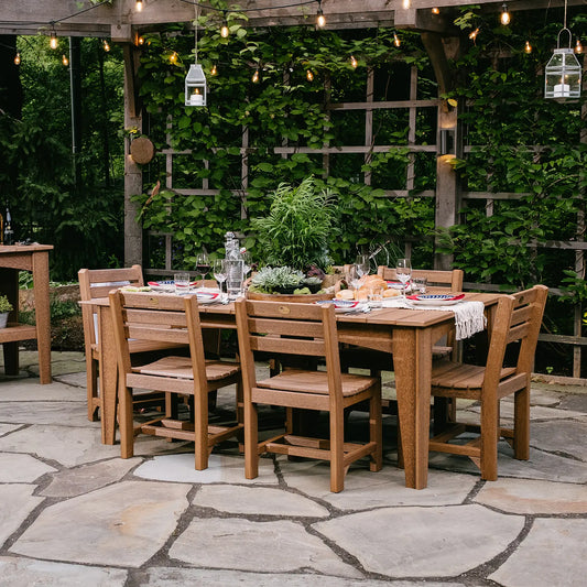 Outdoor dining table with eight chairs, set for a meal on a patio under string lights and greenery.