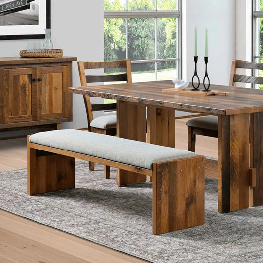 Rustic dining set with cushioned bench on gray rug in a bright room with windows and cabinet.