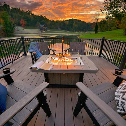 Four Adirondack chairs and a fire pit on a lakeside deck at sunset, with an open book on the table.