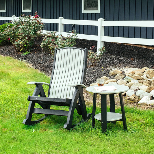Gray Adirondack rocker and side table with drink on grass by white fence, shrubs, and rocks.