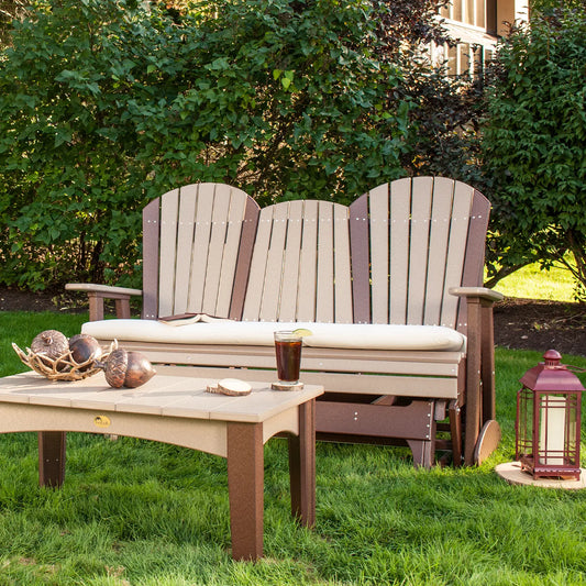 Three-seat Adirondack glider and table on grass by hedge, with sunlit greenery behind.