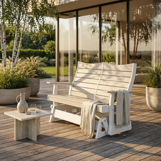 White bench with blanket on wooden deck, glassware table, potted plants, and sunlit doors.