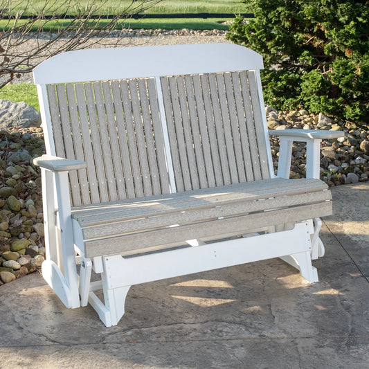 White and gray glider seat on a stone patio, surrounded by rocks, grass, and bushes.