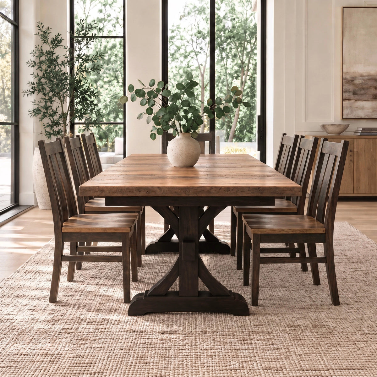 Wooden dining table with six chairs, vase centerpiece, on beige rug near windows and a plant.