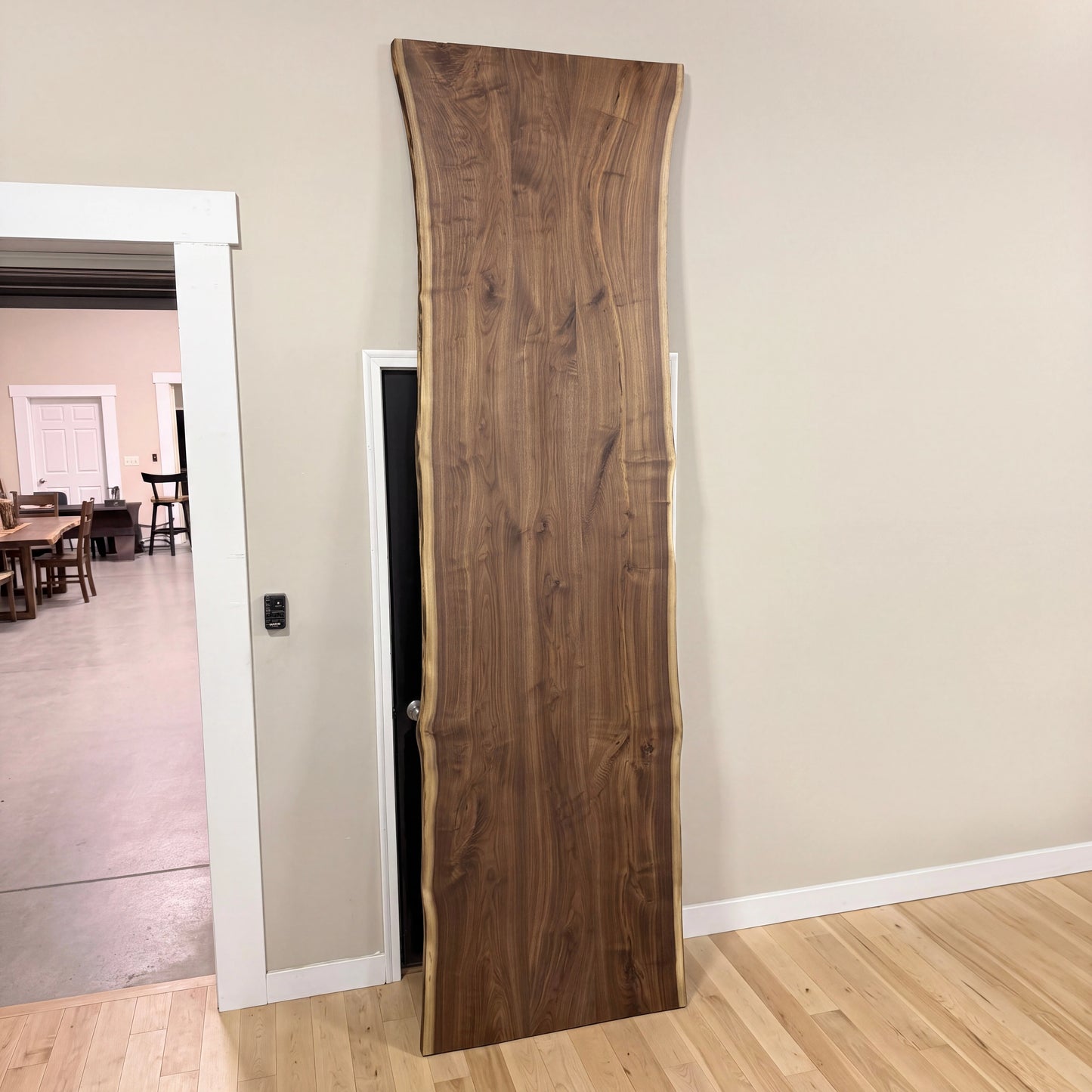 Live edge walnut table leans on beige wall; light floors and open doorway reveal more tables.
