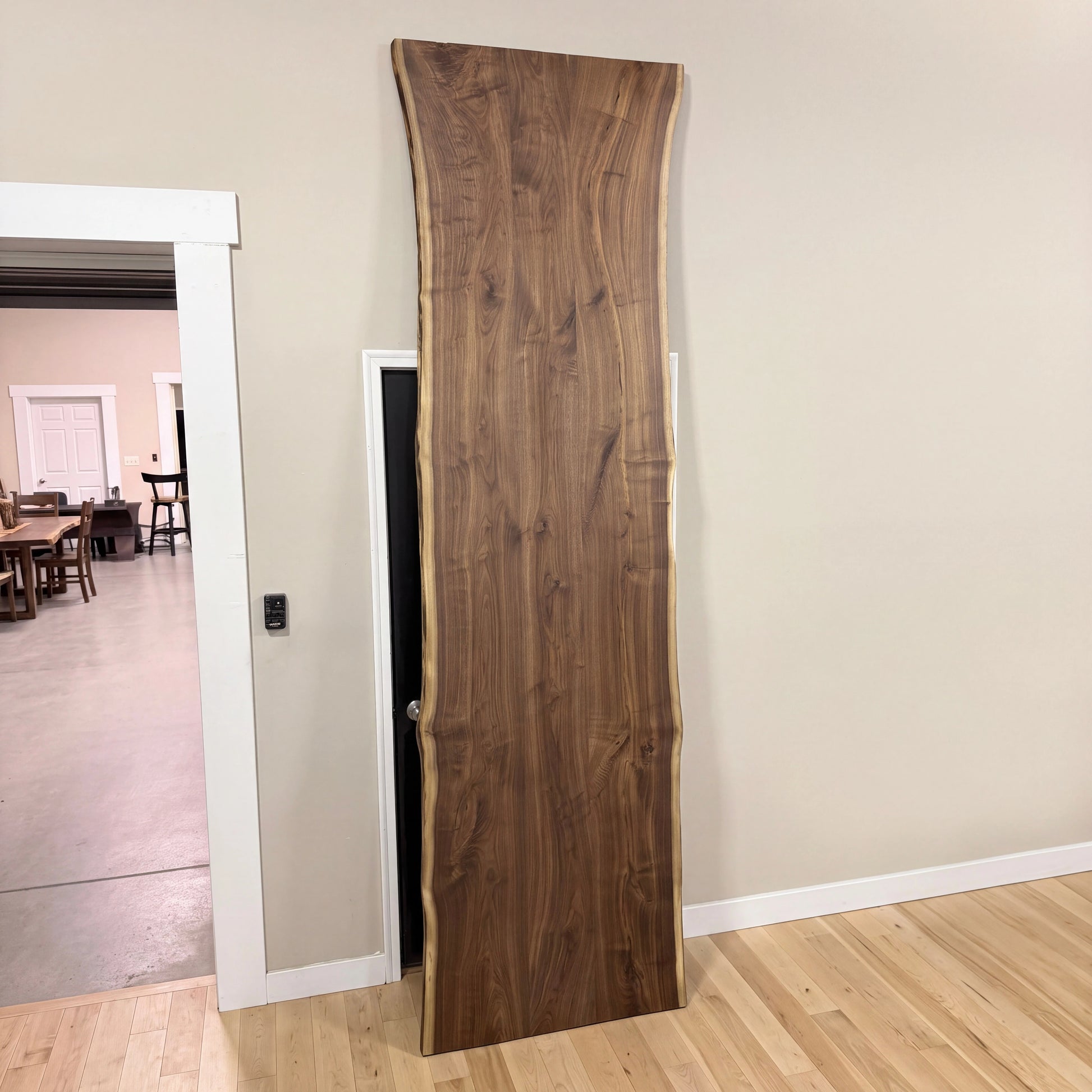 Live edge walnut table leans on beige wall; light floors and open doorway reveal more tables.
