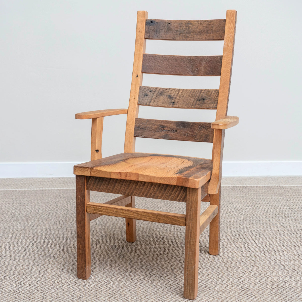 Wooden Akron Ladder Back Chair with arms on light carpet, rustic grain, simple wall behind.