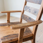 Close-up of rustic Akron Ladder Back Dining Chair with armrests on light wooden floor.