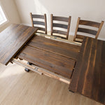 Dining table with partially open leaves, four chairs, on light wood floor near window.