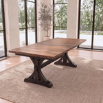 Solid wood dining table on woven rug in bright room with large windows and potted plant.