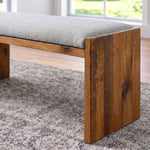 Ethan Wood upholstered dining bench with a gray seat and thick, dark wood slab legs.