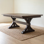 Dark wood dining table on woven rug in bright room with wood floors and light walls.