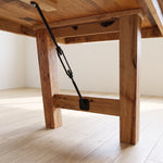 Underside of table with sturdy legs and metal support bar on light wood floor in bright room.