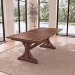 Solid wood dining table with ornate legs on a beige rug in a sunny room with large windows.
