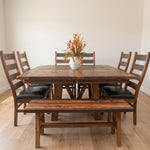 Rustic barnwood dining set with a bench, four black-padded chairs, and dried flowers.