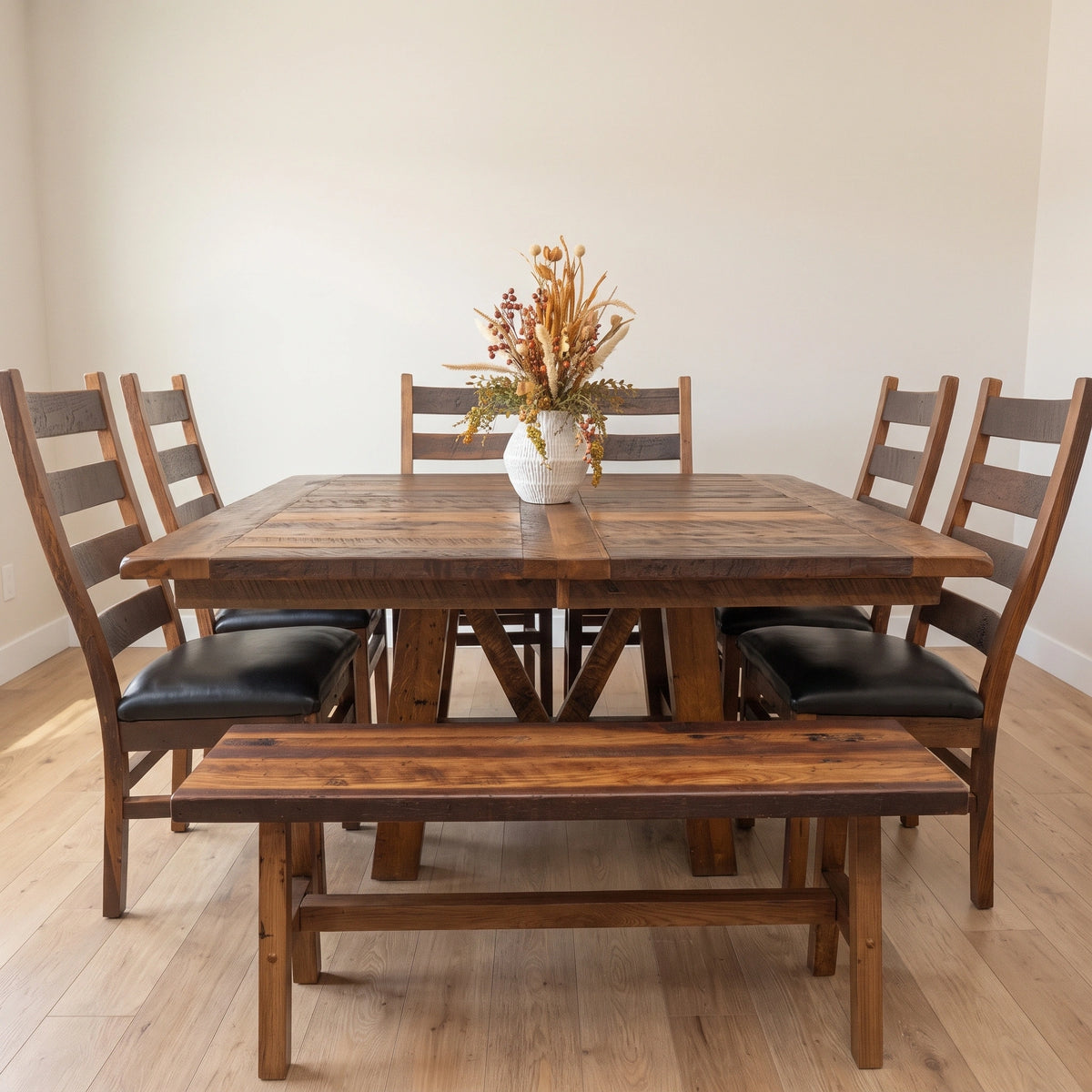 Rustic barnwood dining set with a bench, four black-padded chairs, and dried flowers.