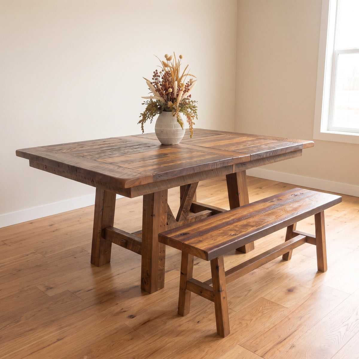 Rustic wood dining table and matching Barnwood bench with a vase of dried flowers.