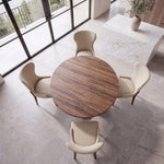 Handcrafted wood dining table with four beige chairs by windows, near marble countertop and vase.