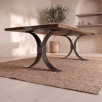 Live edge walnut table with metal legs on a woven rug in a bright room with plant and shelves.