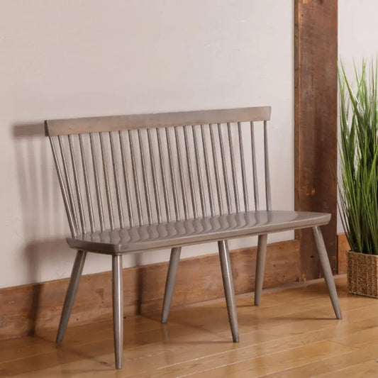 Colby Windsor Bench with spindle back, angled legs; by potted plant on wood floor, driftwood finish.