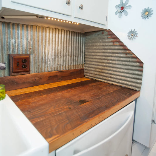 Wood countertop with corrugated metal backsplash, white cabinets, flowers, and outlet nearby.