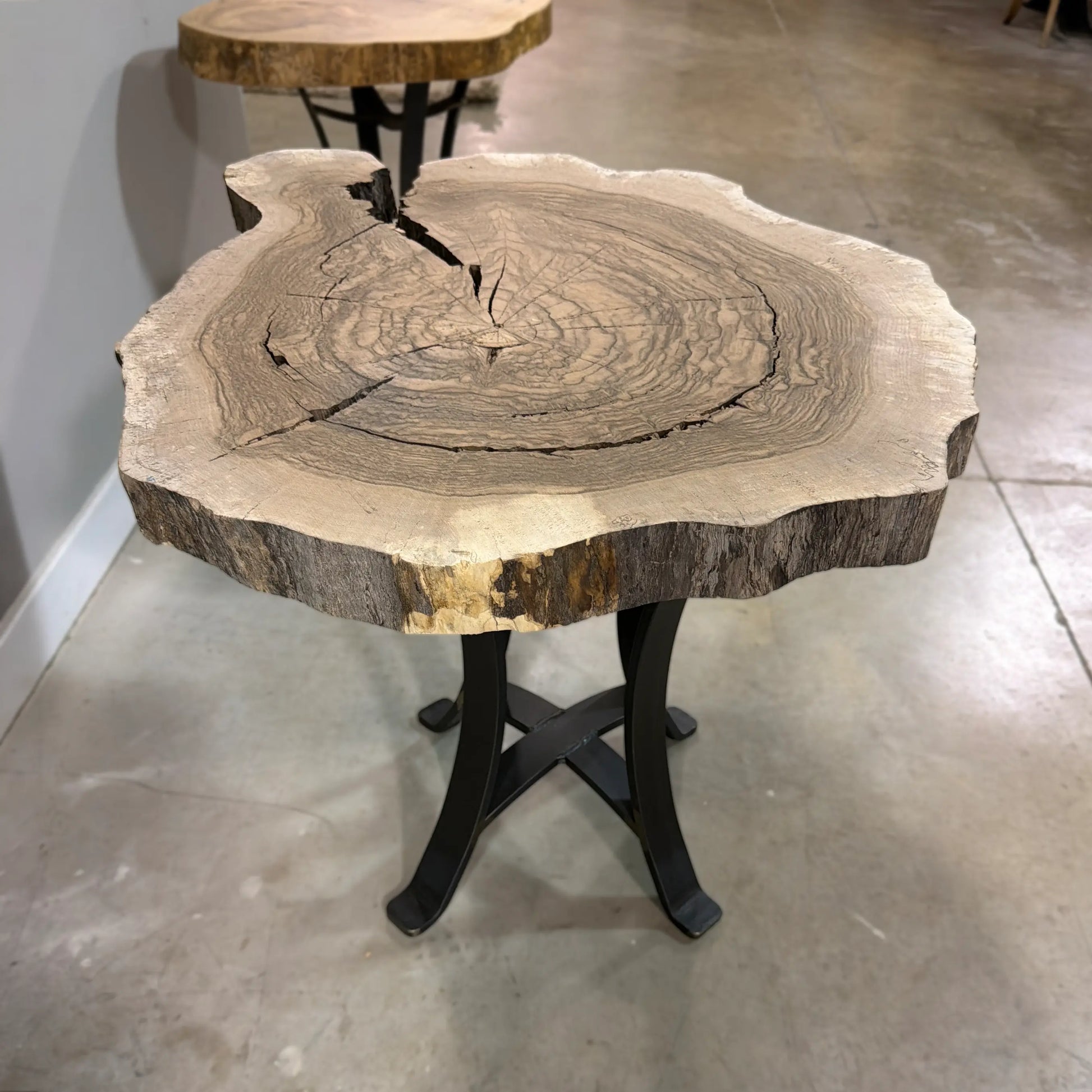 Walnut end table with live edge top, visible rings, steel base on polished concrete floor.