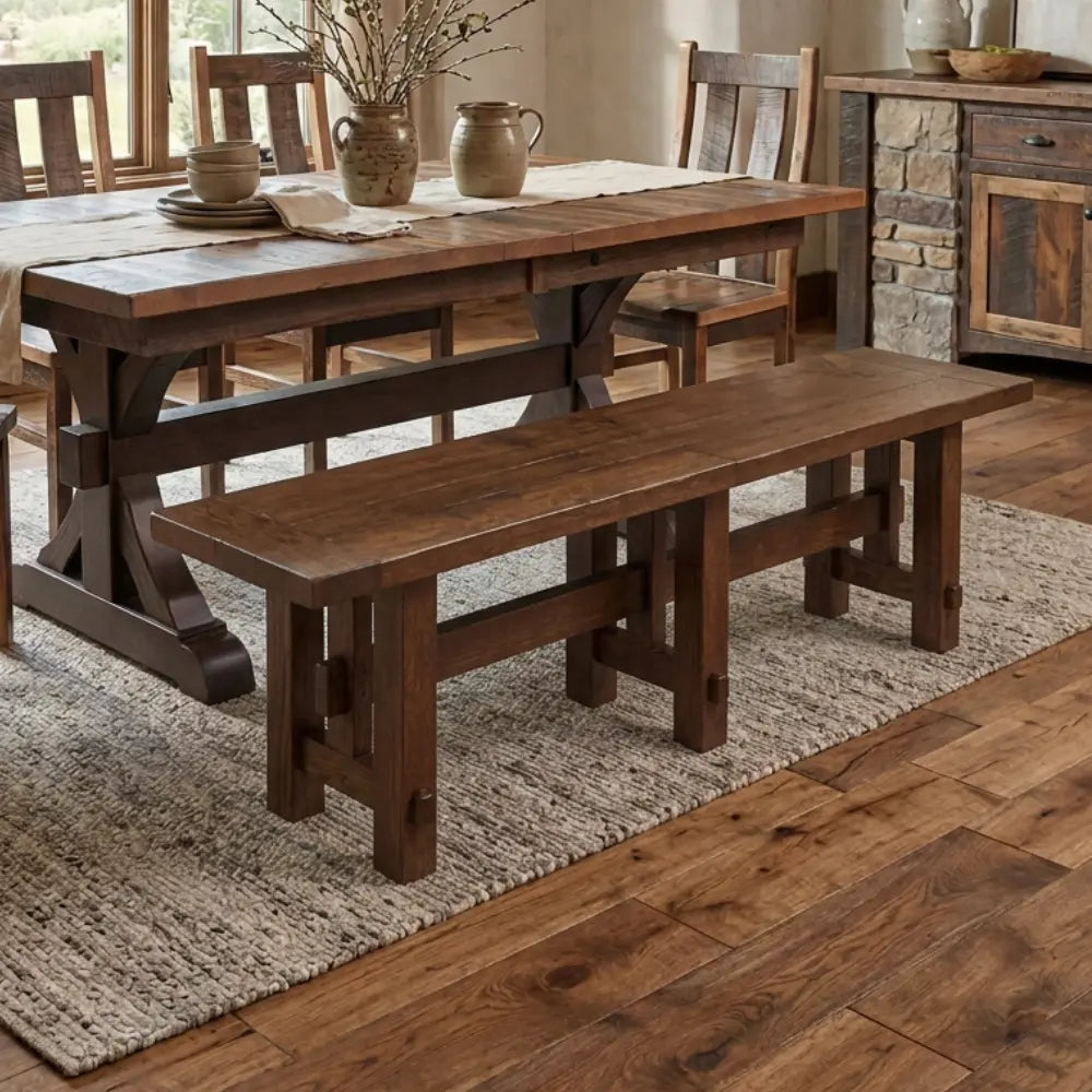 Rustic dining room with a wood table, bench, textured rug, and sunlight on wood floors.