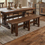 Rustic dining room with a wood table, bench, textured rug, and sunlight on wood floors.