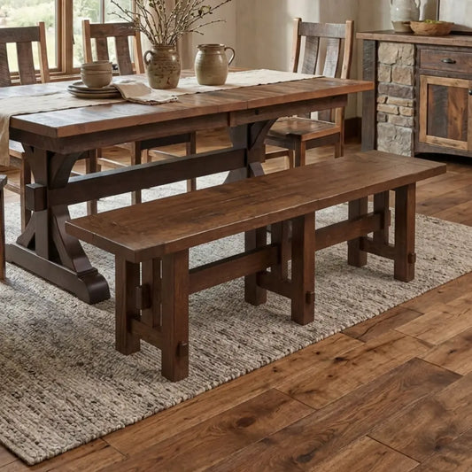 Rustic dining room with a wood table, bench, textured rug, and sunlight on wood floors.