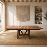 Reclaimed oak dining table on a rug, macramé wall decor, vases, and sunlight through curtains.