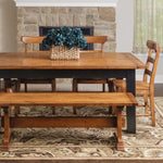 Wood dining set with bench, blue flowers, patterned rug, fireplace and beige-curtained window.