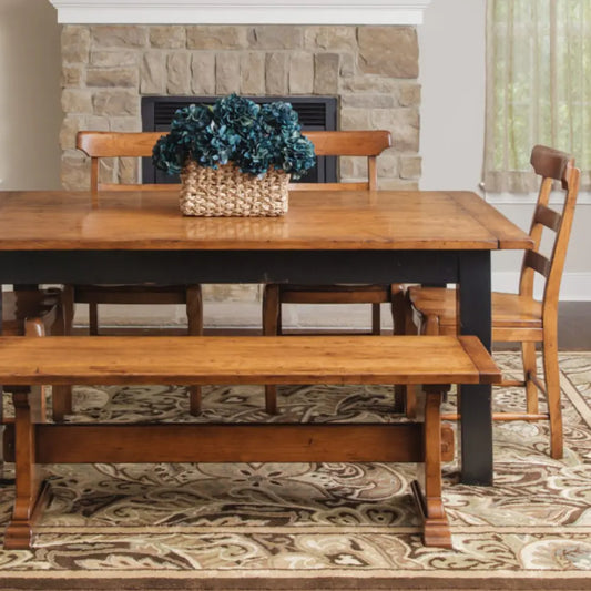 Wood dining set with bench, blue flowers, patterned rug, fireplace and beige-curtained window.