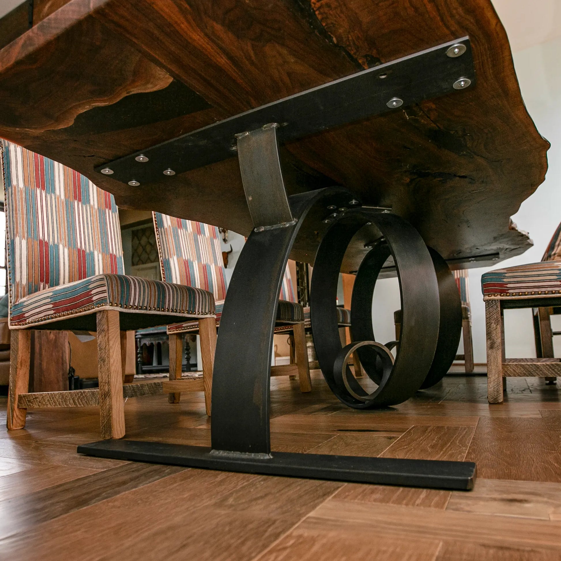 Close-up of a wooden table with metal legs in a room with chairs and a rug.