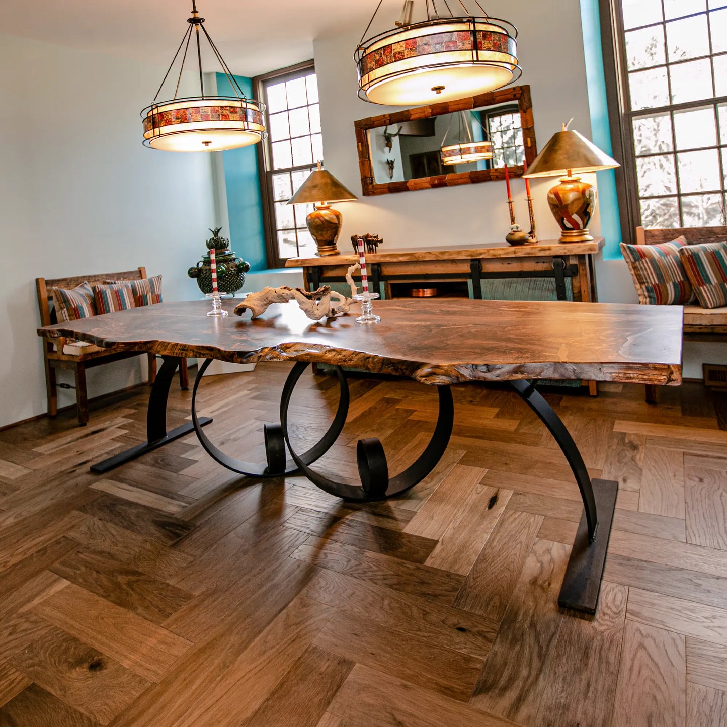 Wooden dining table with metal legs in a room with large windows and decorative lamps.