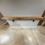 Live edge cherry mantel with black brackets on light wall above polished concrete floor.