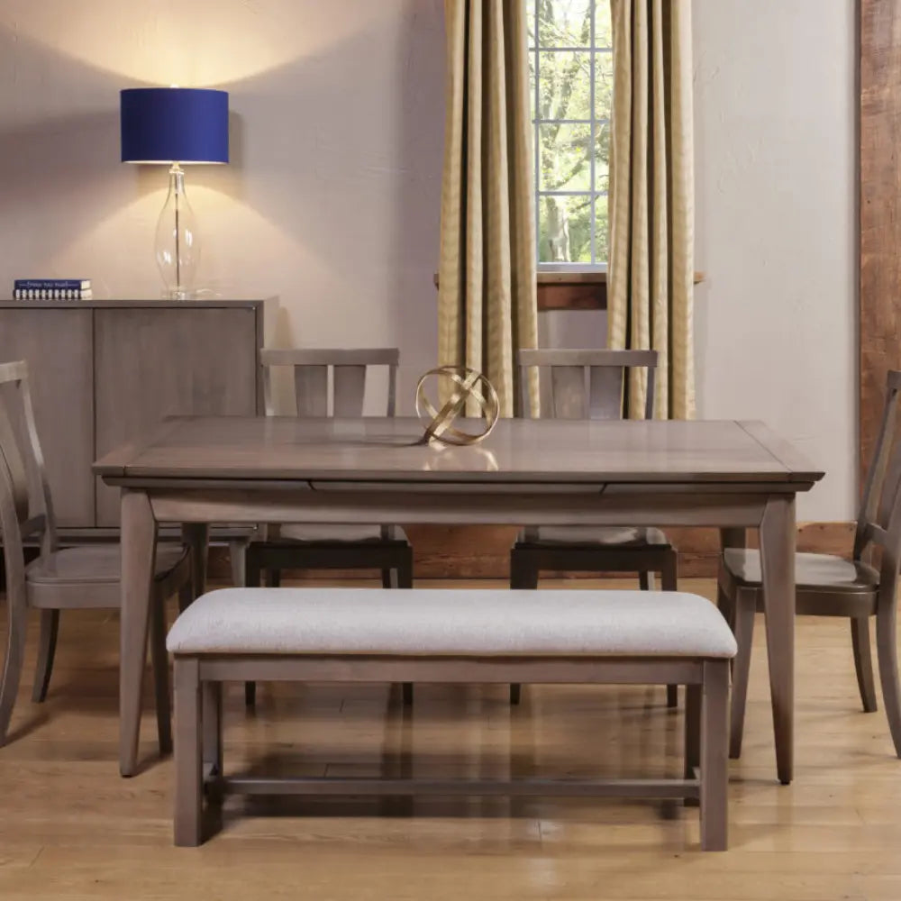 Wood dining table set, upholstered bench, window with curtains, and blue-shaded lamp nearby.