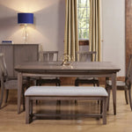 Wood dining table set, upholstered bench, window with curtains, and blue-shaded lamp nearby.