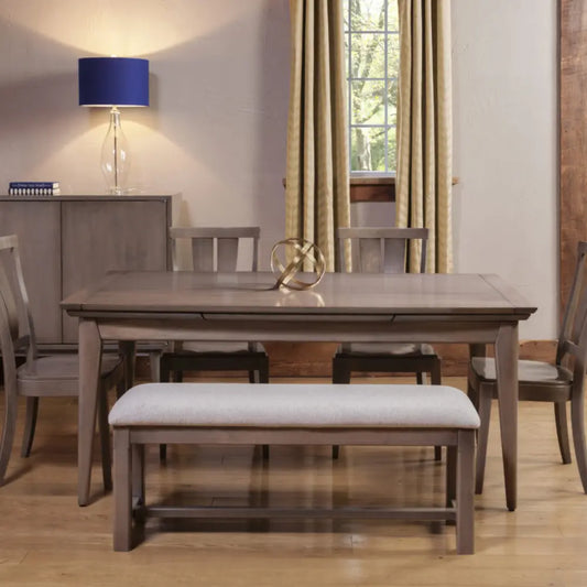 Wood dining table set, upholstered bench, window with curtains, and blue-shaded lamp nearby.
