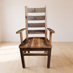 Akron Ladder Back Dining Chair with armrests in a bright, simple room with beige walls.