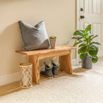 Rustic cherry bench with decor, boots underneath, and plants in a bright entryway.
