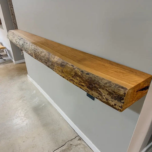 Long live edge cherry wood mantel with rustic finish and bark, mounted on a gray wall above concrete.