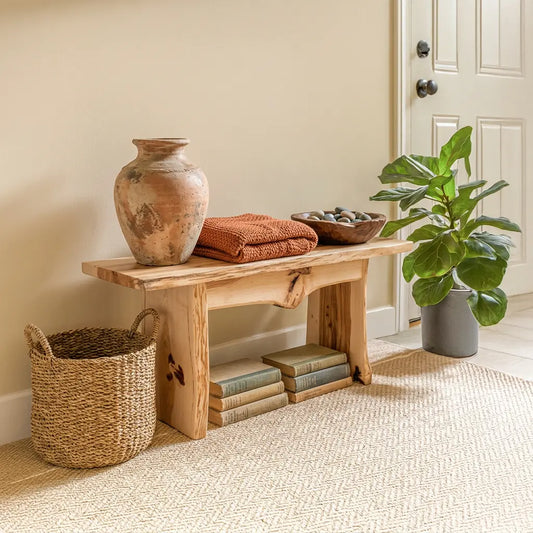 Hickory bench with clay vase, orange towels, baskets, books, and plant in a bright entryway.