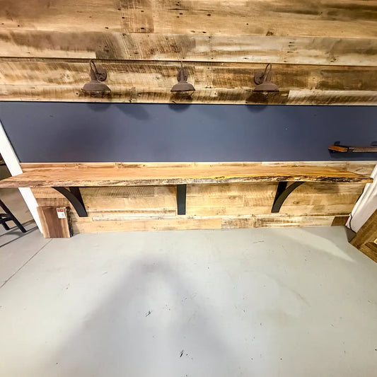 Live edge maple bar top with black brackets on a wood wall under three industrial lights.