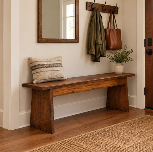 Rustic oak bench with pillow, plant, and hooks holding a jacket and bag in a bright entryway.