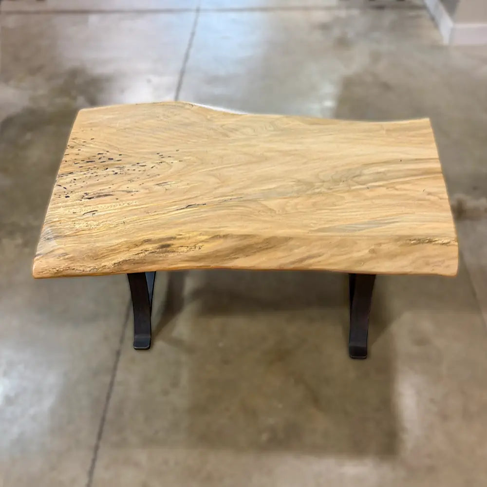 Live edge maple coffee table with steel base on polished concrete floor.