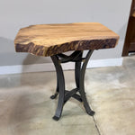 Live edge sycamore end table with steel base on concrete floor, set against a plain wall.
