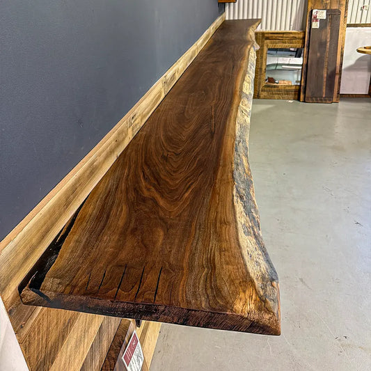 Live edge walnut bar top with rich grain on gray floor, custom wood table visible behind.