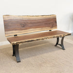 Live edge wood bench with back and black metal legs on beige rug against a white wall.